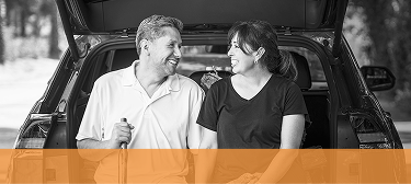 A smiling couple sitting together in the open back of a car.
