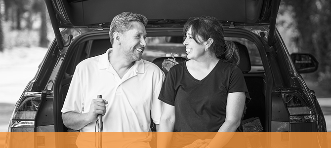 A smiling couple sitting together in the open back of a car.